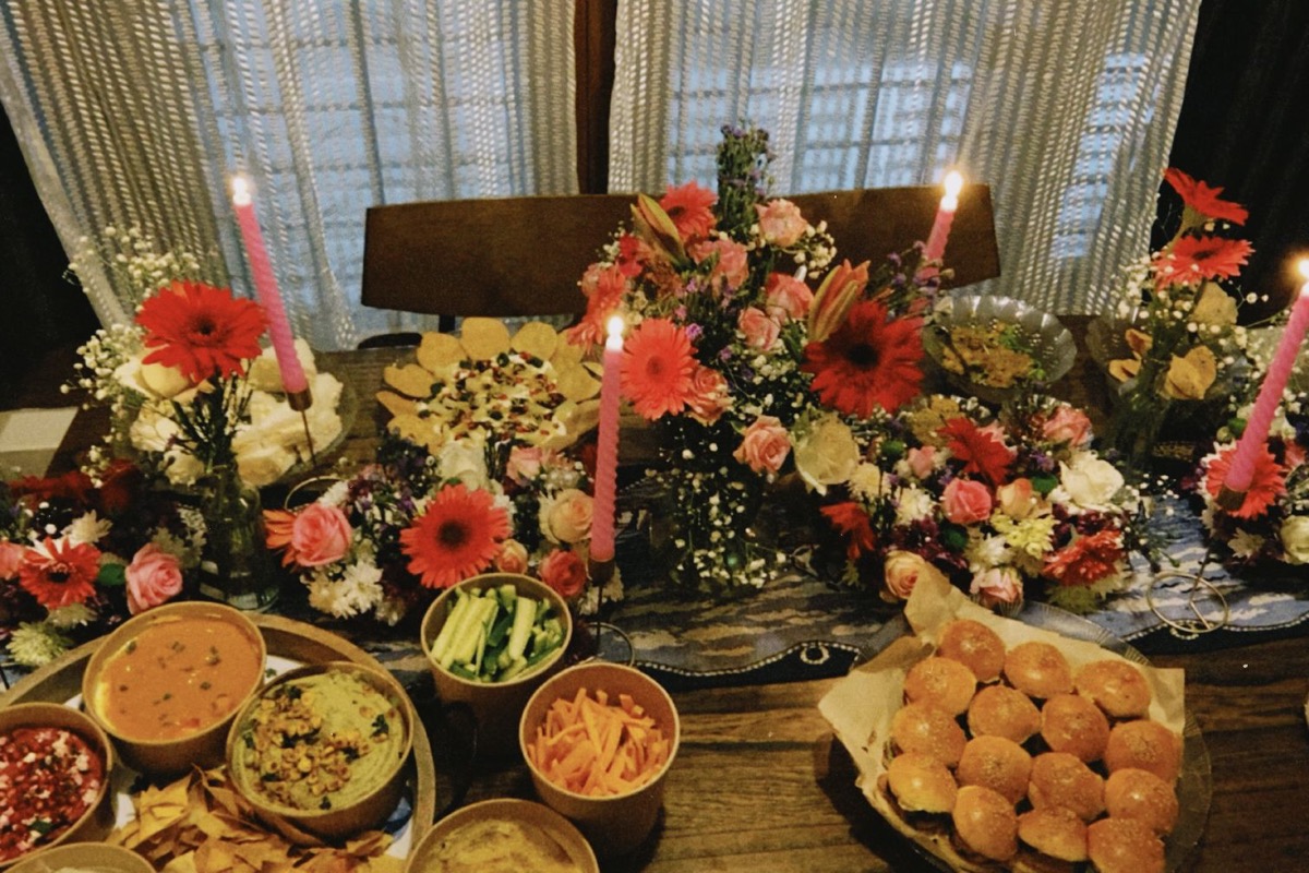 A candlelit birthday grazing table styled by Pooja — hummus boards, lavash chips, papdi chaat, sliders, and a flower runner with pink taper candles